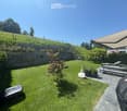 Well-maintained garden with a lawn, a small tree, potted plants, outdoor furniture including a bench and a table, and a covered patio area.