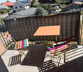 Balcony with a table and colorful folding chairs, surrounded by a metal railing and a privacy screen, overlooking a residential area.