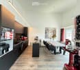 Modern kitchen with dark wooden cabinets, stainless steel appliances, a central island, and a dining area with a wooden table and chairs. Features a red sewing machine as a decorative element, a vase with flowers, and a painting on the wall.