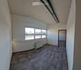 Empty room with tiled floor, white walls, large windows, radiator, and a door leading to another space.