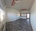Empty room with tiled floor, white walls, and a large window with blinds. There is a door leading to another space.