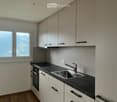 Modern kitchen with white cabinets, black countertop, stainless steel sink, and faucet. Features a window with a scenic view.