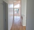 Bright, modern hallway with wooden flooring, white walls, built-in closet, and a view to a balcony area through large glass doors.