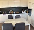 Modern kitchen with white cabinets, stainless steel appliances, a white dining table with four grey chairs, and various kitchen items on the counter.