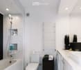 Modern bathroom with white tiles, bathtub, toilet, sink, towel rack, and small potted plants on the counter.
