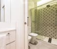 Modern bathroom with a glass-enclosed shower, toilet, and towel on a rack. The shower has a decorative tile pattern, and the bathroom features white fixtures and a sleek design.