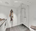 Modern bathroom with white tiled walls, a glass-enclosed shower, a sink with a mirror, a toilet, and a washing machine. Towels and a bathrobe are neatly arranged on the counter and toilet seat.