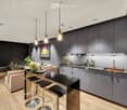 Modern kitchen and living area with grey cabinets, pendant lights, a sofa, coffee table, and bar stools.