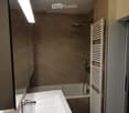 Modern bathroom with a white sink, chrome faucet, bathtub, showerhead, and a white radiator. The walls are tiled in beige, and the ceiling has a round light fixture.