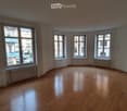 Empty room with wooden flooring and large windows, featuring radiators under the windows.