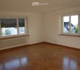 Empty room with wooden flooring, white walls, large windows with blinds, and radiators beneath the windows.