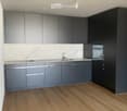 Modern kitchen with grey cabinets, marble backsplash, wooden flooring, and a stainless steel sink.