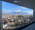 Balcony with a modern glass railing, overlooking a town with houses and distant snow-capped mountains.