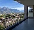 Balcony with a metal railing, overlooking a town with houses and mountains in the background.