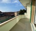 Balcony with tiled floor, green metal railing, and view of neighboring buildings and trees.