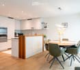 modern kitchen, island countertop, white cabinets, wooden flooring, built-in oven and microwave, dining table and chairs, artwork