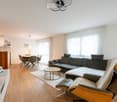 light walls, light wood floor, table and chairs in dining area, sofa, coffee table, TV stand, picture frame, mirror