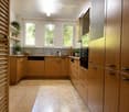 Modern kitchen with wooden cabinets, stainless steel appliances, and a central island. Features a sink, oven, dishwasher, and various kitchen items on the counter.