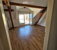 Empty attic space with wooden flooring, exposed wooden beams, and a door leading to a balcony.