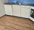 Modern kitchen with white cabinets, a dishwasher, a sink with a faucet, and wooden flooring.