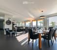 Modern dining and living area with dark tiled flooring, large windows, a dining table with chairs, a sofa, coffee table, and decorative items.