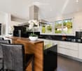 Modern kitchen with white cabinets, wooden island, black countertops, and stainless steel appliances. Features include a wine rack, mixer, and decorative flowers on the island.