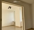 Empty room with light-colored tiled flooring, white walls, and a large window allowing natural light. Features a radiator and a ceiling light fixture.