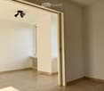 Empty room with beige tiled flooring, white walls, and a large open doorway leading to another space. A small window and radiator are visible in the adjacent area.