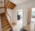Bright hallway with wooden staircase, open doors leading to living and dining areas, modern interior design.