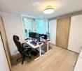 A modern, well-lit office space with a large window, a standing desk, ergonomic chair, multiple computer screens, and various office supplies.