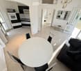 Modern living and dining area with large windows, a black sofa, a white dining table with chairs, a coffee table, and a mirror on the wall.