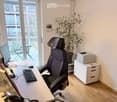 Modern office space with a large window offering a view, a desk with a computer setup, a comfortable office chair, a printer on a small cabinet, and a potted plant.