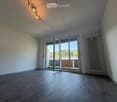 Empty room with wooden flooring, white walls, large sliding glass doors leading to a balcony, and a radiator on the wall.