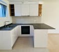 Modern kitchen with white cabinets, black countertops, a sink, and an oven. Features a window with a view and a wooden shelf on the right side.