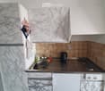 Modern kitchen with marble-patterned cabinets, stainless steel sink, electric kettle, and various cleaning supplies on the counter.
