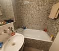Bathroom with a white sink, bathtub, and mosaic tile walls. A mirror above the sink, and towels hanging on the side.