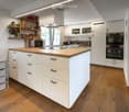 Modern kitchen with white cabinets, wooden island, microwave, oven, fridge, blender, and shelves with various items.