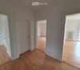 Empty room with wooden flooring, white walls, and multiple doors leading to other spaces.
