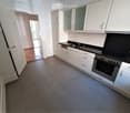Modern kitchen with white cabinets, black countertops, and stainless steel appliances including an oven and dishwasher. The floor is tiled, and there is a visible doorway leading to another room.