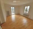 Empty room with wooden flooring, white walls, and large windows offering a view of the cityscape.