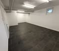Empty room with white walls, dark tiled floor, and a small window. No furniture or equipment present.