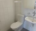 A small, clean bathroom with white tiled walls, a toilet, a sink with a mirror, and a white cabinet above the sink.