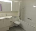 Modern bathroom with white tiles, a double sink vanity, a toilet, a bathtub with a showerhead, and a large mirror above the sink.