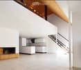 Open-plan living and kitchen area with white walls, a fireplace, a bench, and a staircase leading to an upper level.