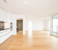 Bright, open-plan space with light wooden flooring, white cabinetry, and large glass doors leading to a balcony. The room is empty, with no furniture or appliances visible.