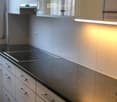 Modern kitchen with white cabinets, black countertop, and built-in induction cooktop. Features sleek stainless steel handles and ambient lighting.