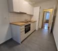 Modern kitchen with white cabinets, wooden countertop, sink, and built-in oven. The space is clean and well-lit, with a hallway leading to another room visible in the background.