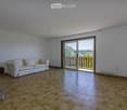 Bright living room with wooden tiled flooring, white walls, a cream-colored sofa, and a sliding glass door leading to a balcony.