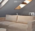 A cozy attic living space with a cream-colored sofa, a small round table, and chairs, illuminated by skylight windows.