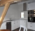 Modern kitchen with white cabinets, stainless steel appliances, a sink, and a window. A wooden chair is visible in the foreground.